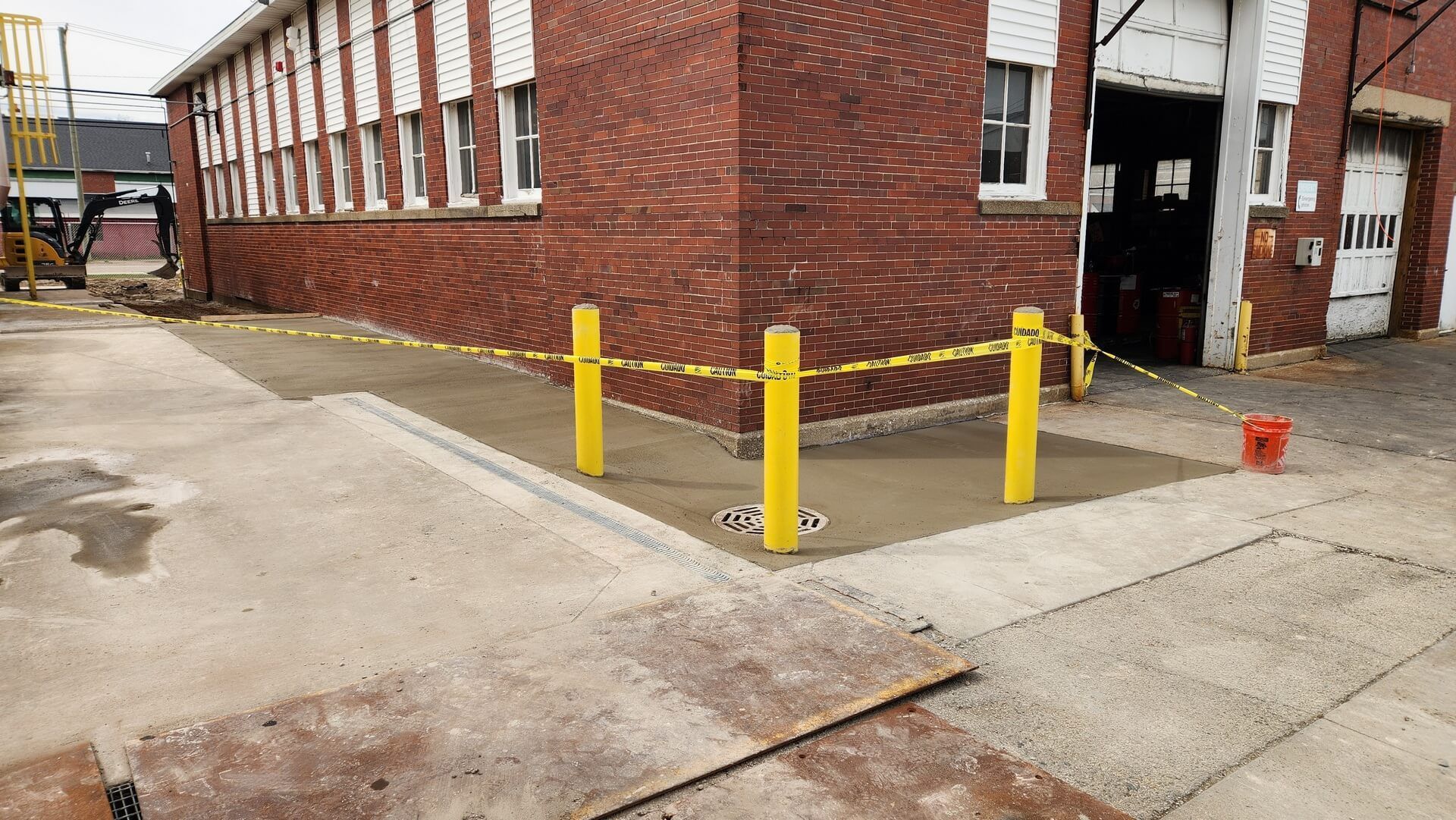 Brick building corner with new concrete, yellow posts, and caution tape.