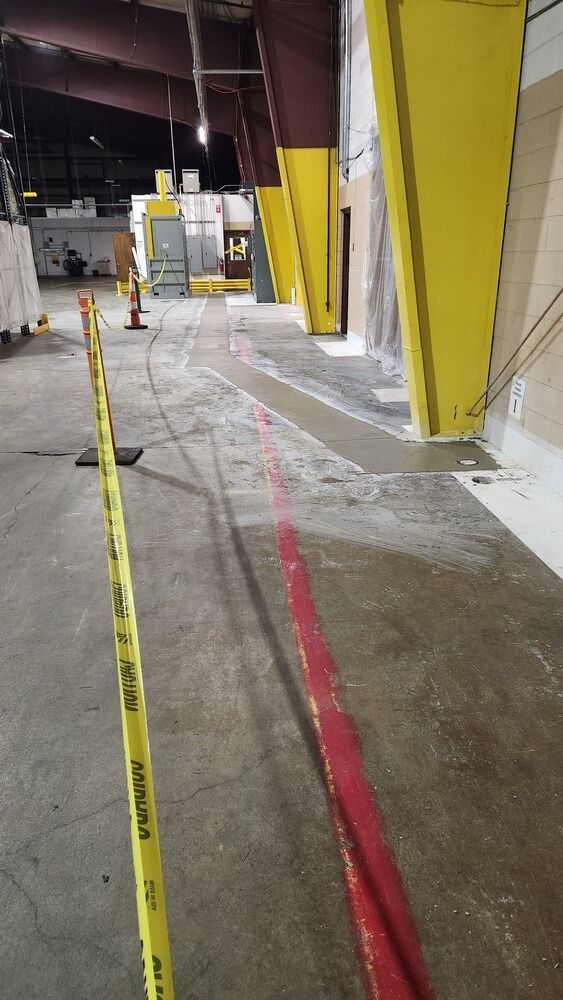A warehouse floor with a red line painted down the middle, yellow support beams, and caution tape.