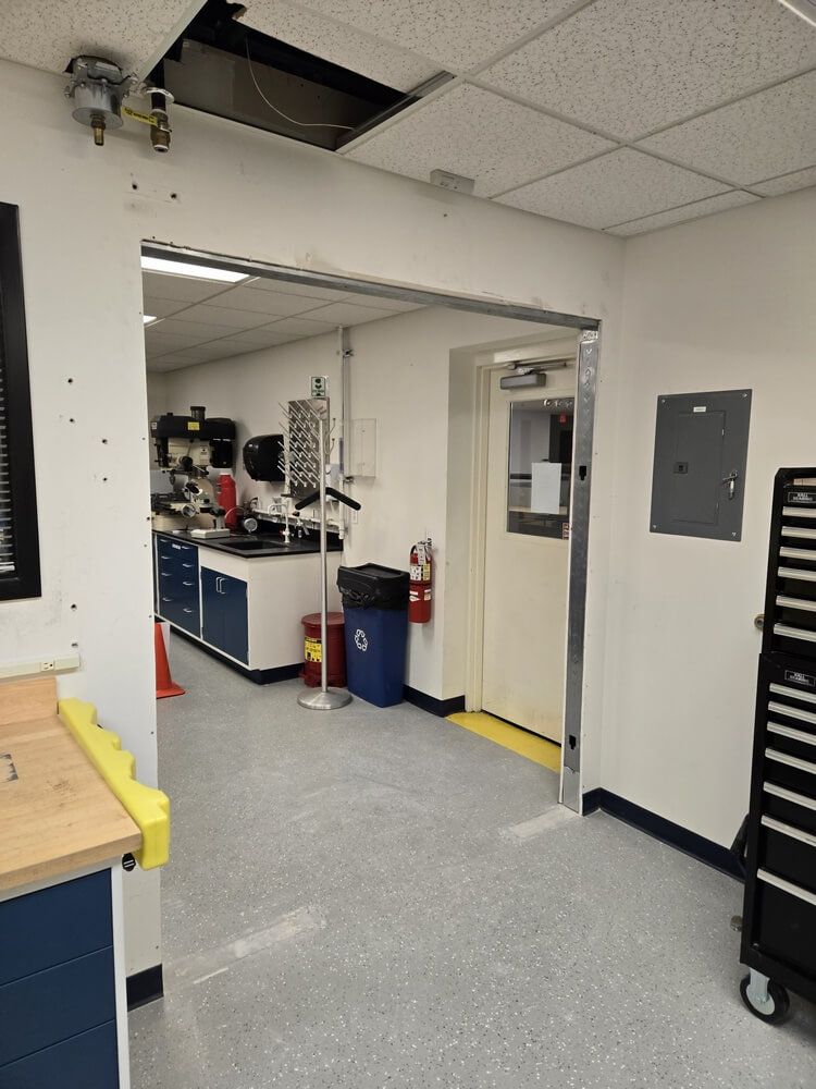 Hallway with a doorway leading to a lab area. White walls, gray floor, and blue and red equipment.
