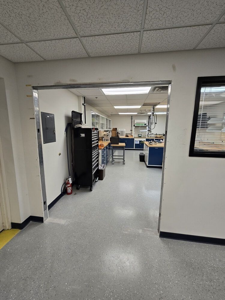 View into a workshop from a doorway. Tools, workbenches, cabinets, and a fire extinguisher are visible.