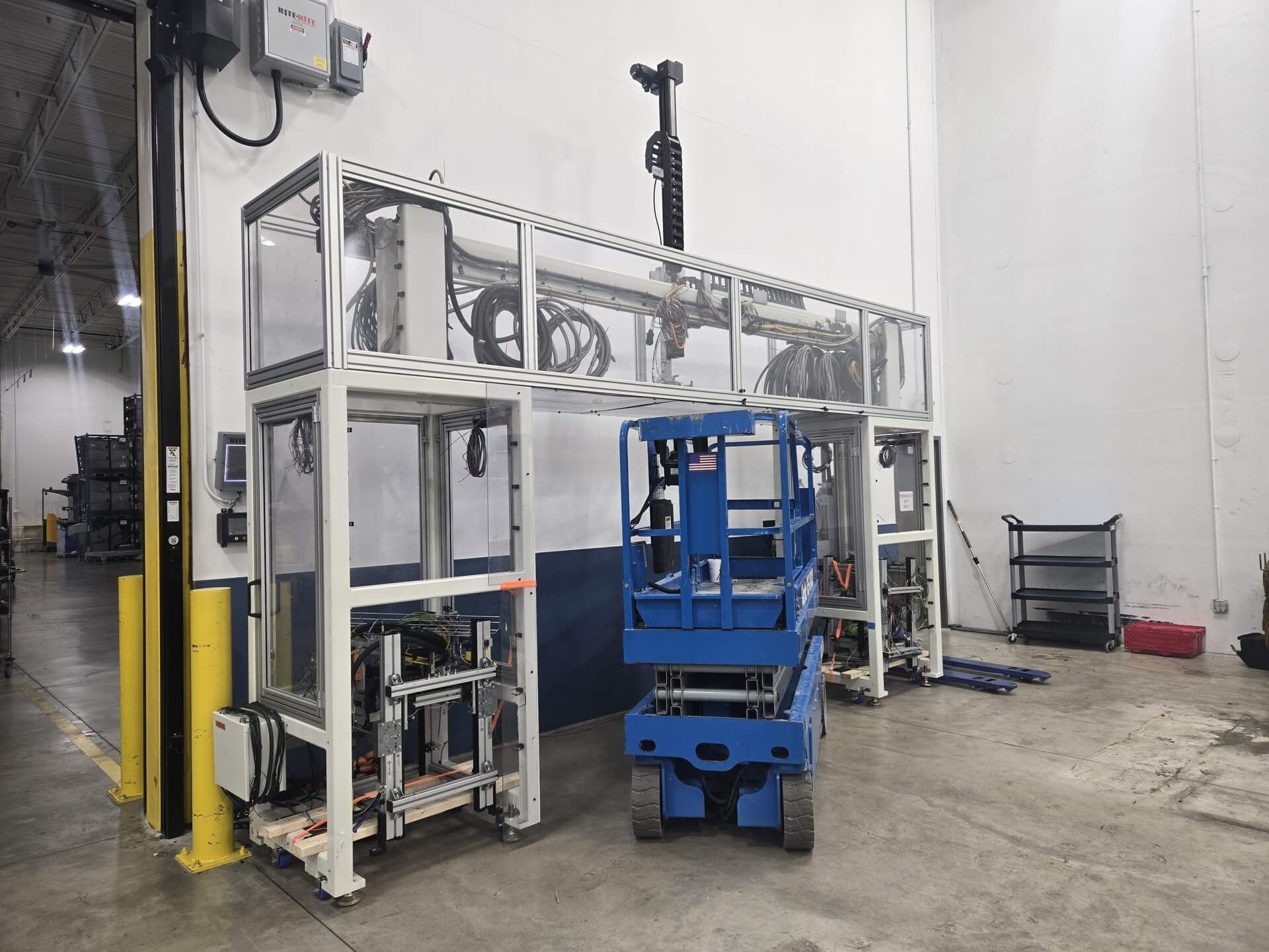 White automated assembly line with a blue scissor lift inside a warehouse.