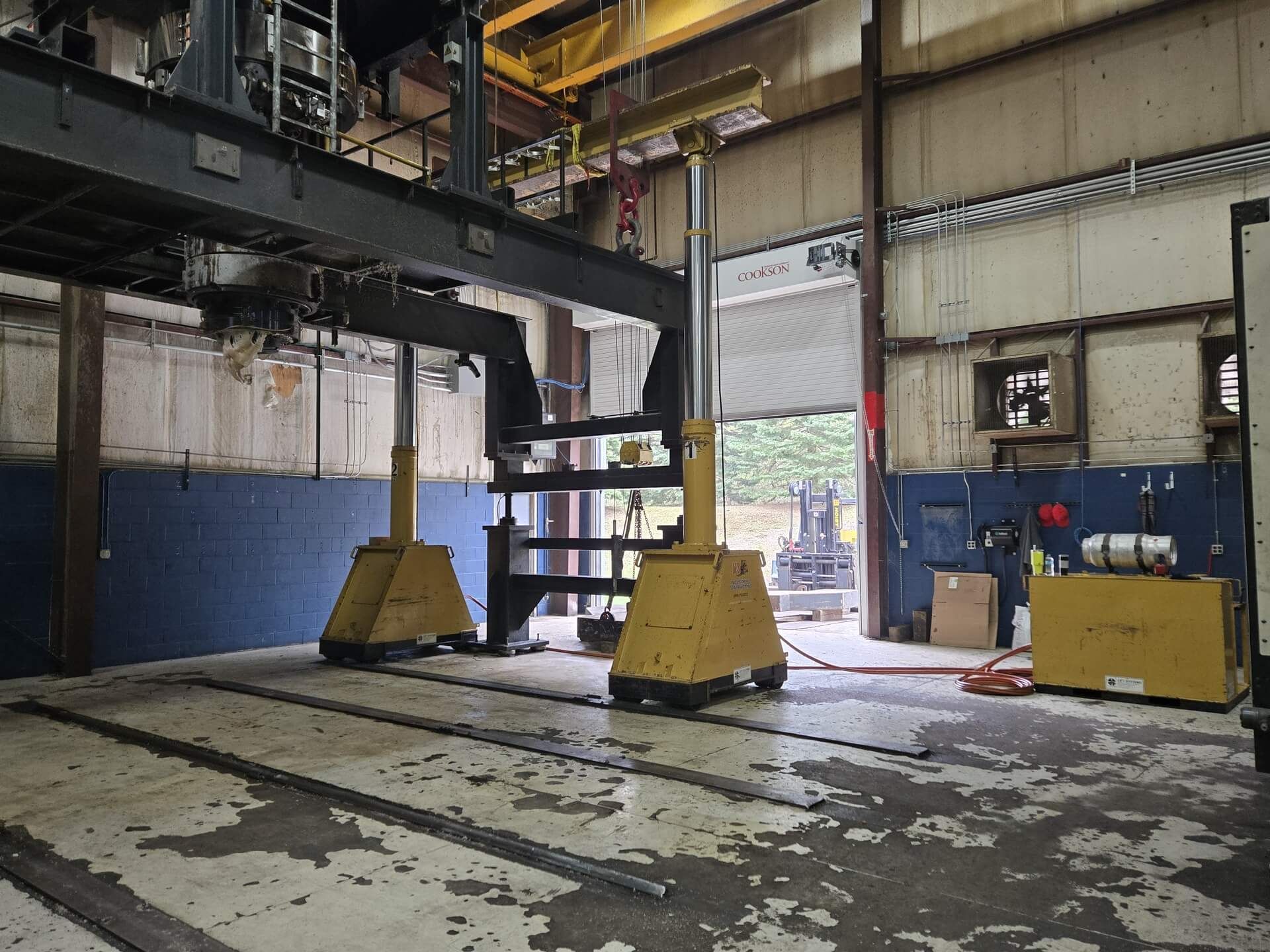 Yellow supports under a large metal structure inside a warehouse, with an open door.