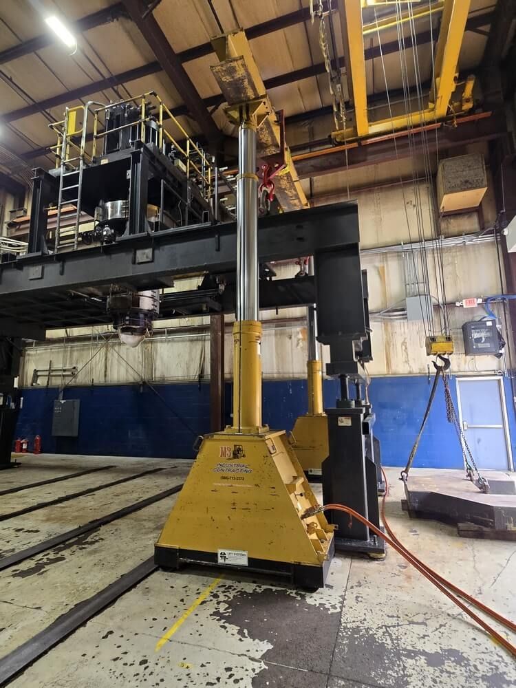 Yellow industrial lift in a warehouse. Overhead crane and metal beams are visible.