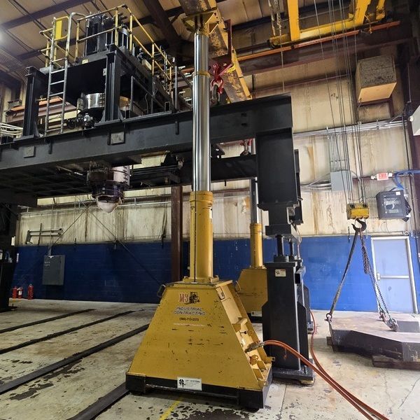 Yellow industrial lift next to a large black machine in a factory.