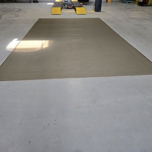 A rectangular concrete repair patch on a gray shop floor, near a vehicle lift.