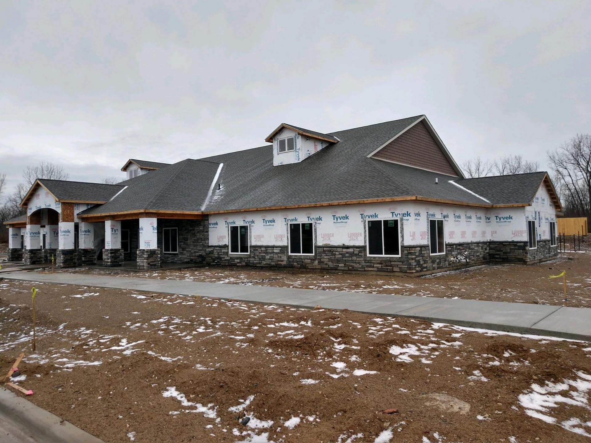 Building under construction with stone siding, dark roof, and windows, on a snowy day.