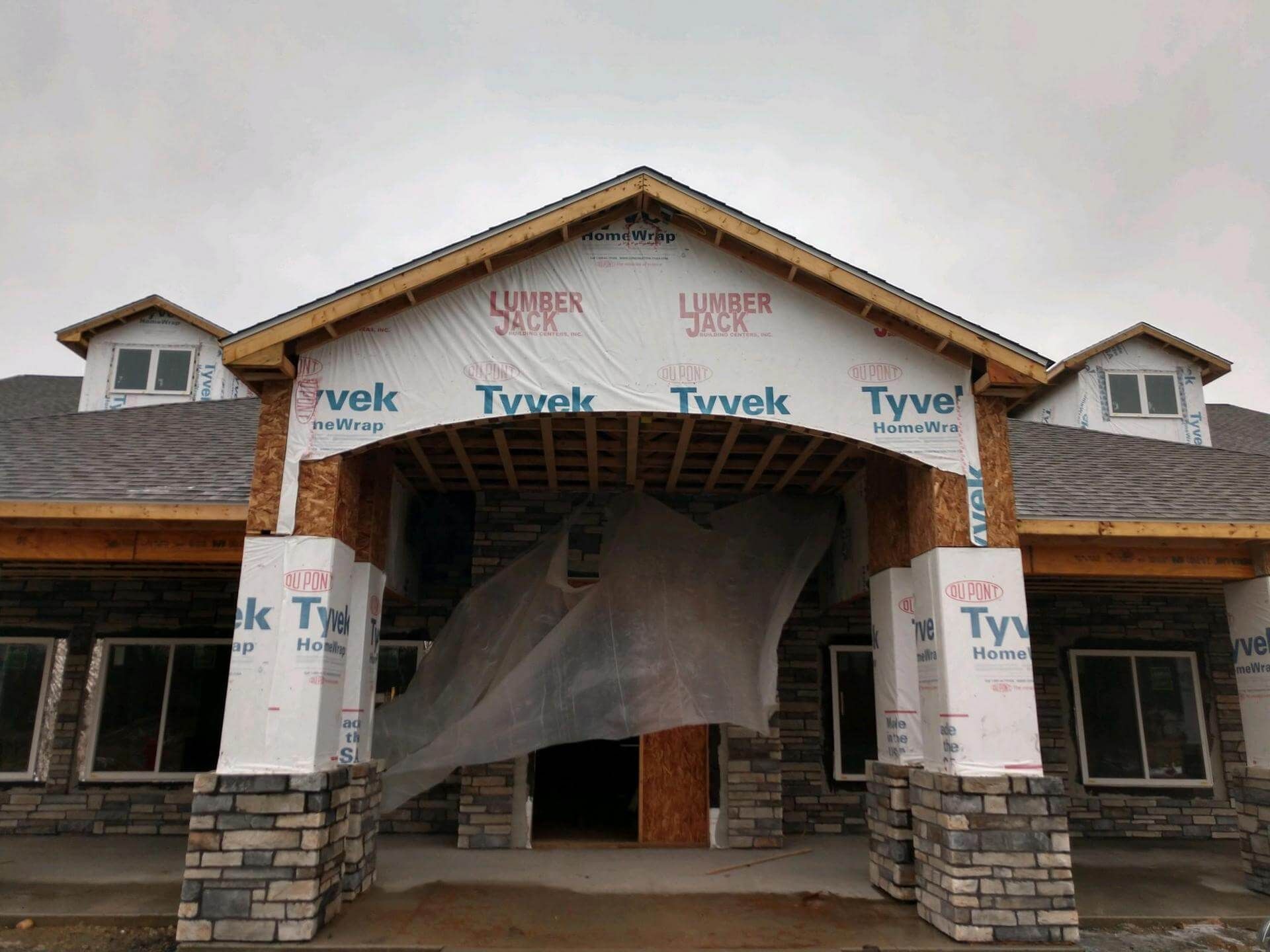 Building under construction; stone and wood facade with Tyvek wrap, under overcast sky.