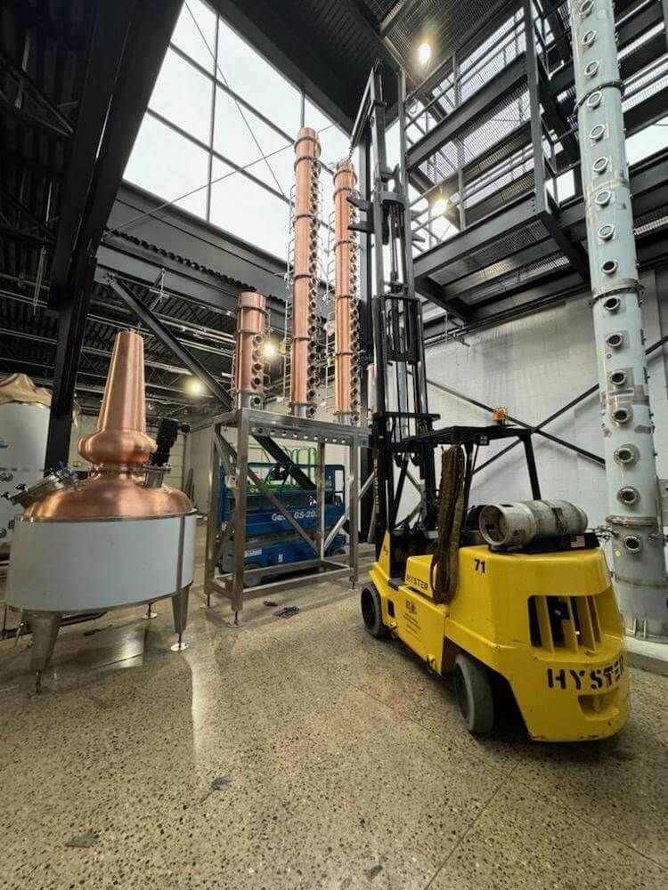 Yellow forklift in a distillery, copper stills, and industrial setting.