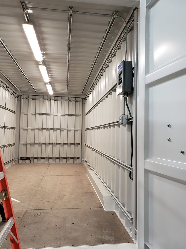 Interior of a white room with corrugated walls. Lighting fixtures and electrical conduit run along the ceiling and walls.