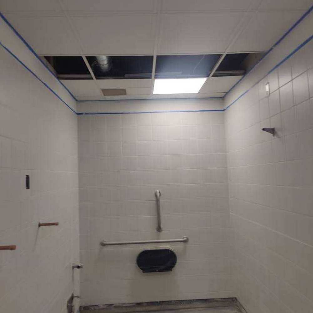 Empty white tiled shower with missing ceiling tiles and grab bars.