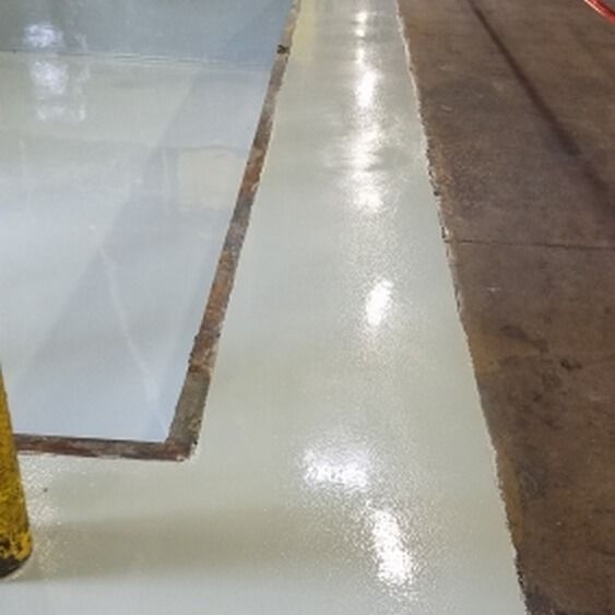 Light grey epoxy-coated industrial floor, glossy surface, adjacent to concrete floor section and unfinished area.