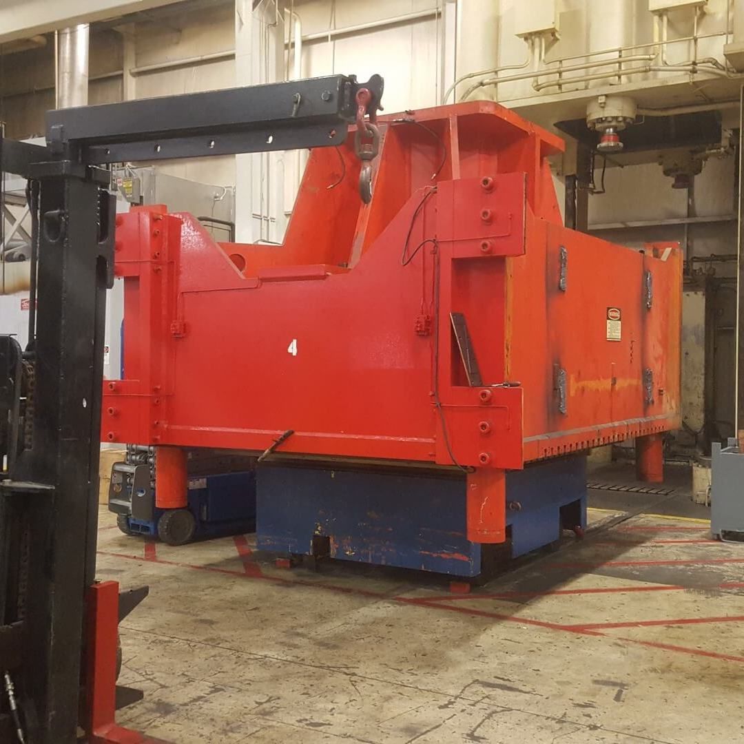 Large red industrial machinery on a blue base, near a forklift, in a factory setting.