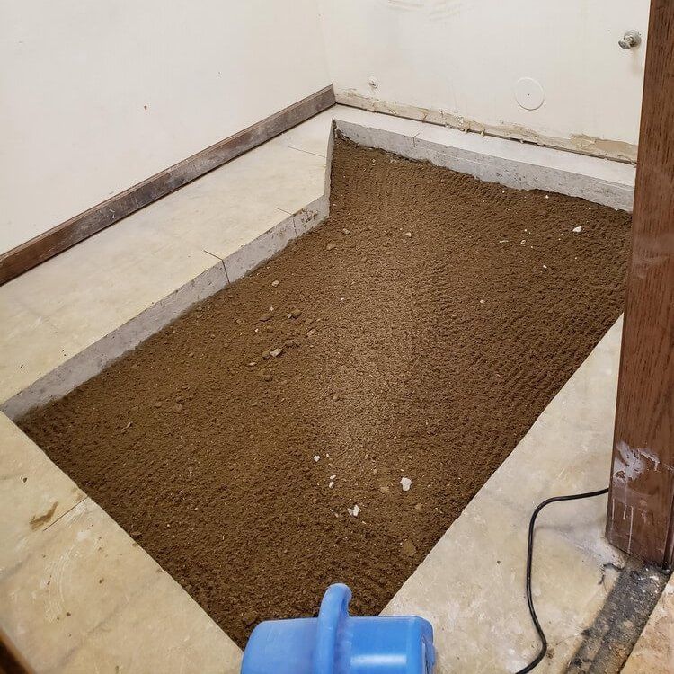 Interior room, excavated floor filled with brown material, surrounded by concrete border and walls.