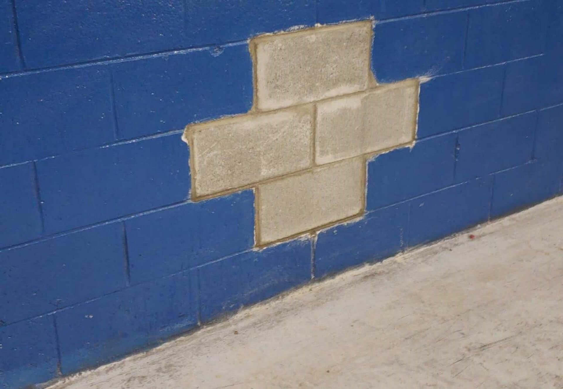 Blue painted cinder block wall with unpainted section in a cross shape. Concrete floor.