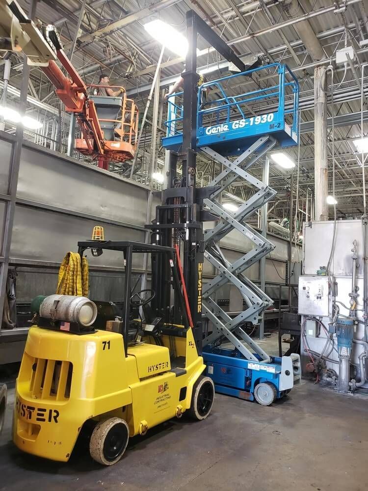 Yellow forklift and blue scissor lift inside a large industrial facility. Another lift is in the background.
