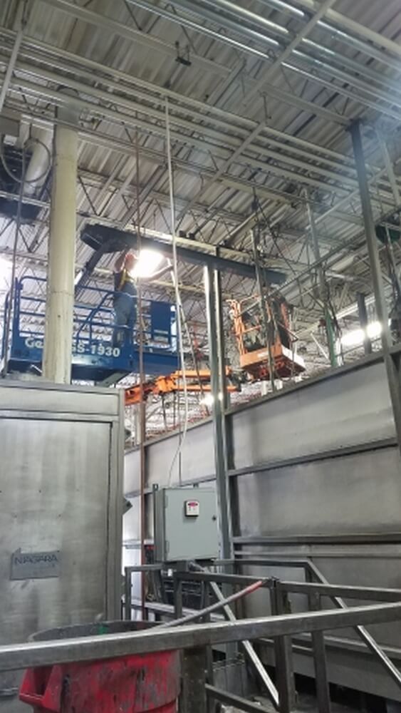 Two lifts with workers inside, working on ceiling pipes in an industrial building.