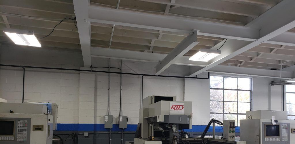 A manufacturing facility with machinery, a high ceiling, and large windows.