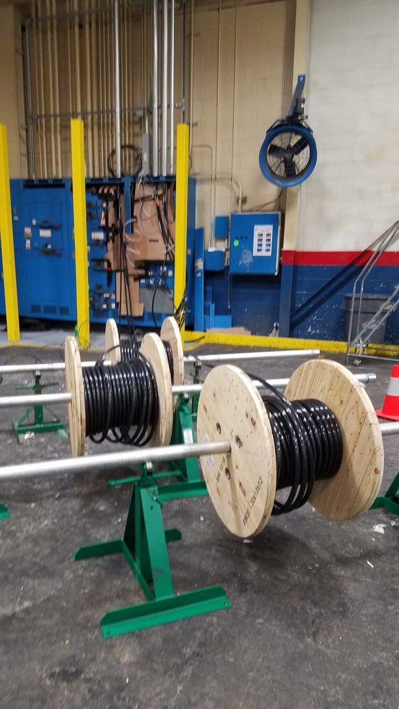 Three spools of black cable on green metal stands in an industrial setting.