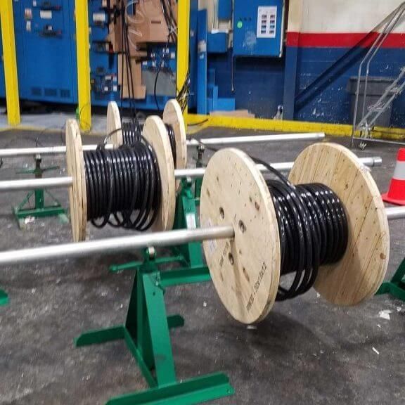Spools of black cable on green metal stands in an industrial setting.