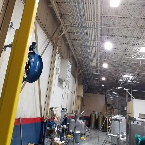Interior of a factory, with overhead pipes and equipment. A worker is present.