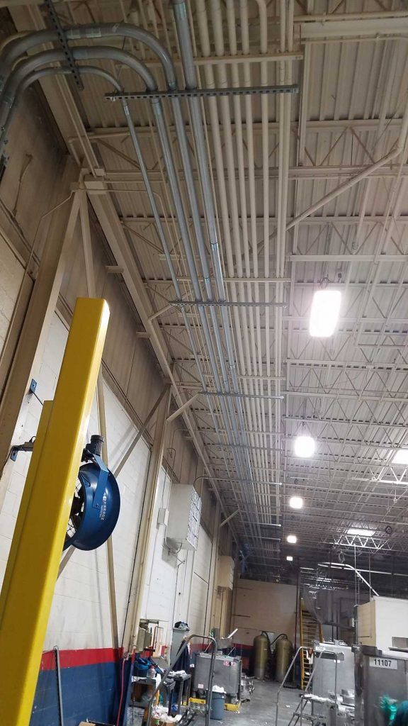 Ceiling with electrical conduits, lighting in a large industrial building.