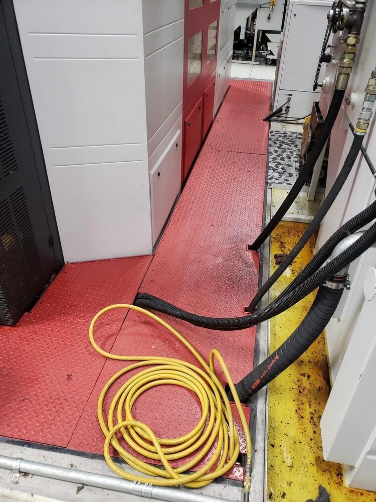 Yellow coiled cord on red mat with black hoses alongside a cabinet. Floor shows water and oil stains.