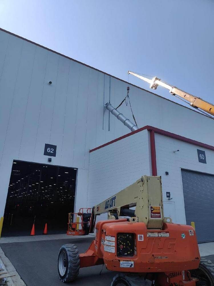 An orange JLG boom lift and crane working on the side of a white warehouse with open door.