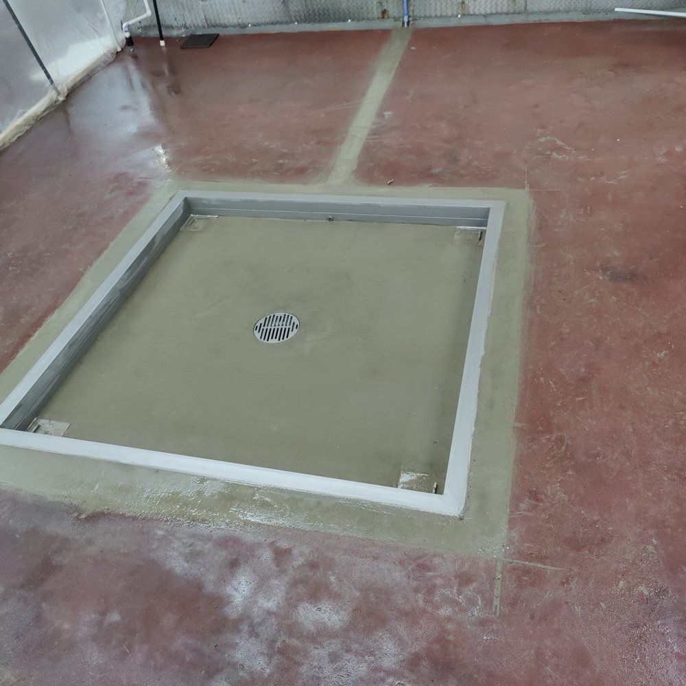 Square shower drain with metal frame set in a red-brown concrete floor.