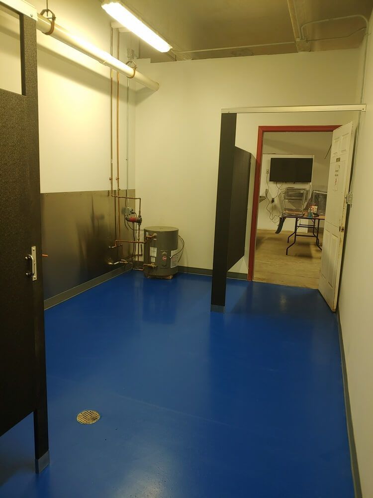 A small, blue-floored room with a toilet, sink, and an open doorway to another room with equipment.