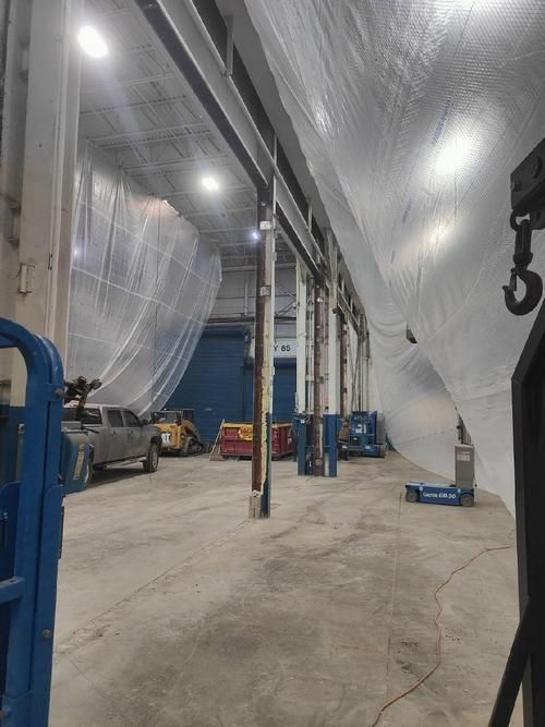 Large warehouse interior with white tarps hanging from the ceiling and construction equipment.
