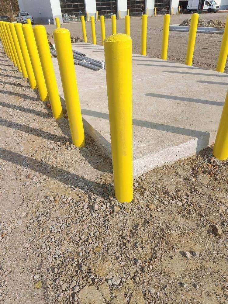 Yellow bollards line a concrete pad, on gravel ground, near a building with garage doors.