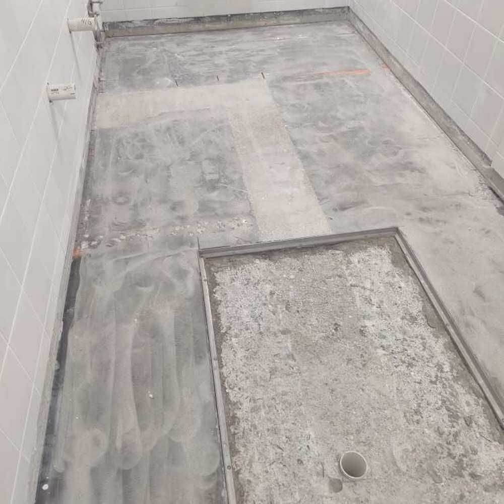 Concrete shower floor with a drain and tiled walls.