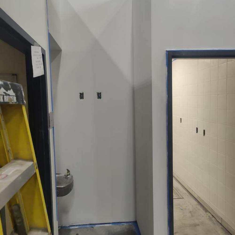 Bathroom interior with painted walls, a drinking fountain, and open doorways. A ladder stands by the left doorway.