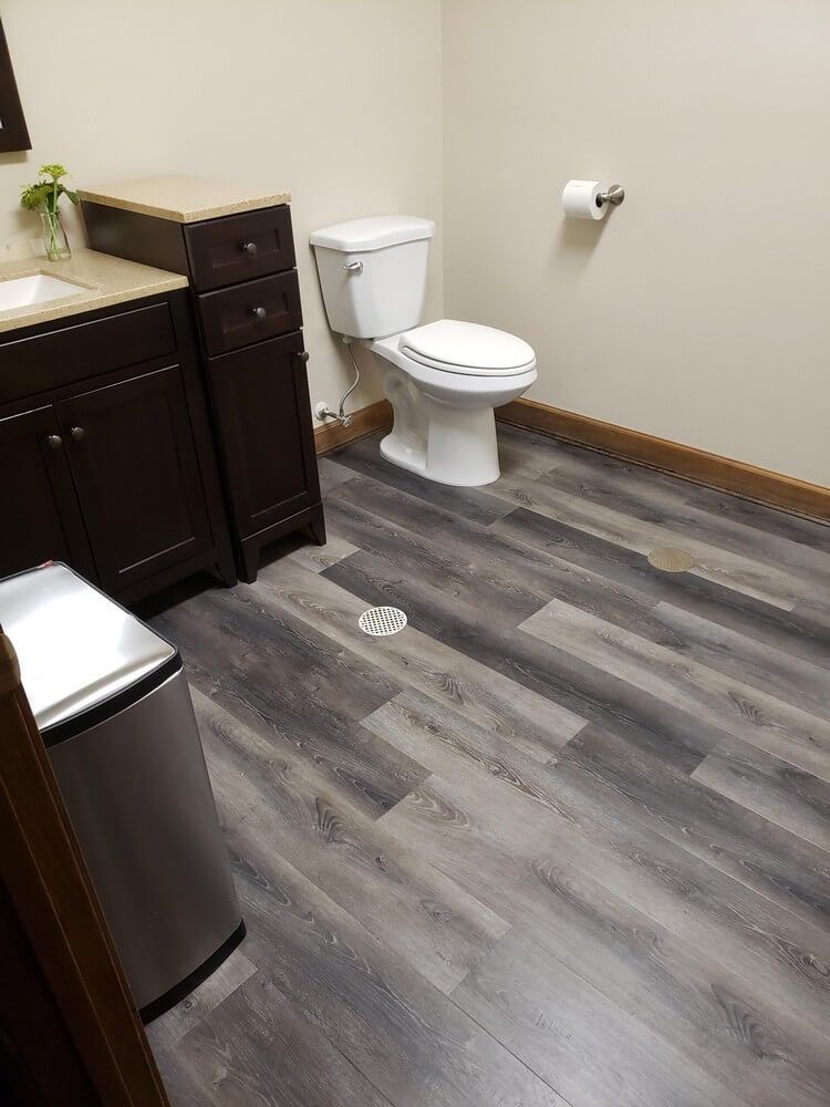 Bathroom with a dark brown vanity, white toilet, and gray wood-look flooring.