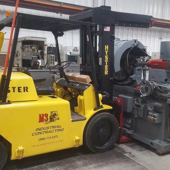 Yellow forklift lifting industrial machinery inside a factory.