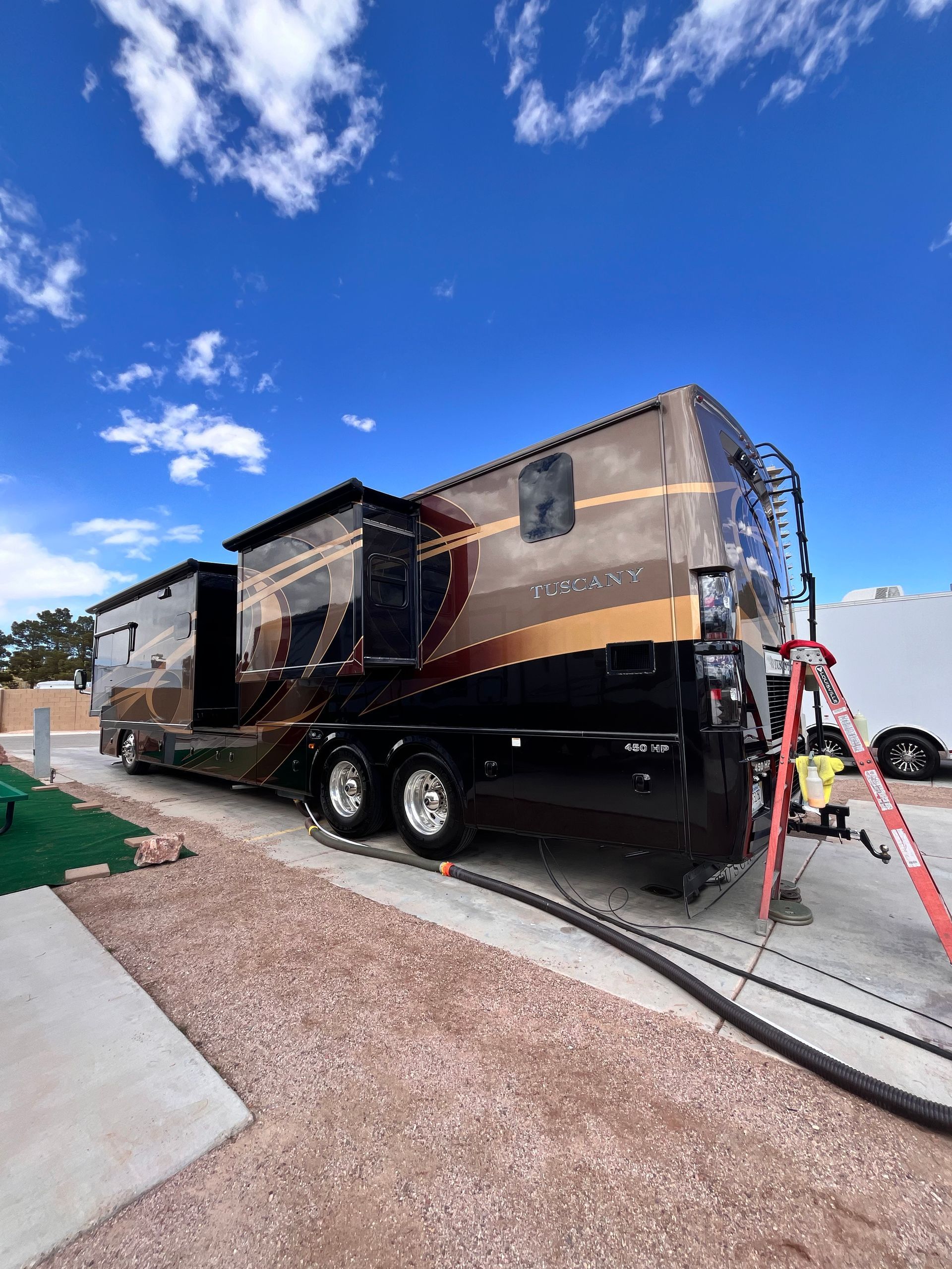 A large rv is parked in a parking lot next to a ladder.