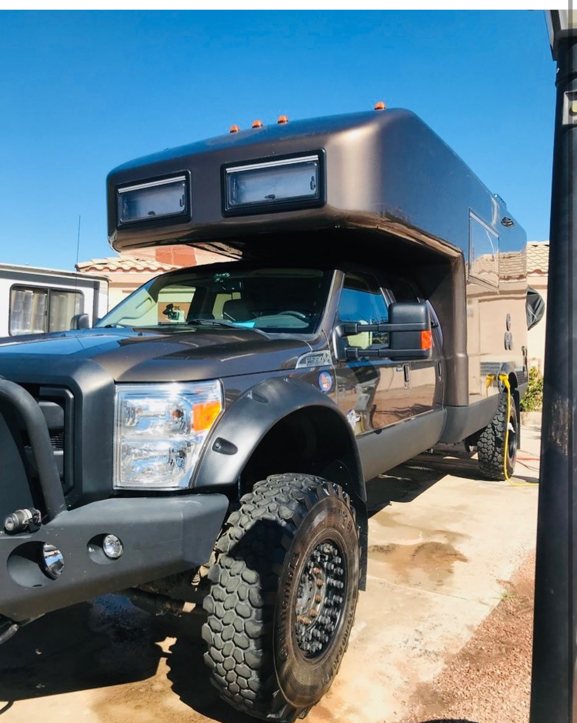 A black truck with a camper on top of it is parked on the side of the road.