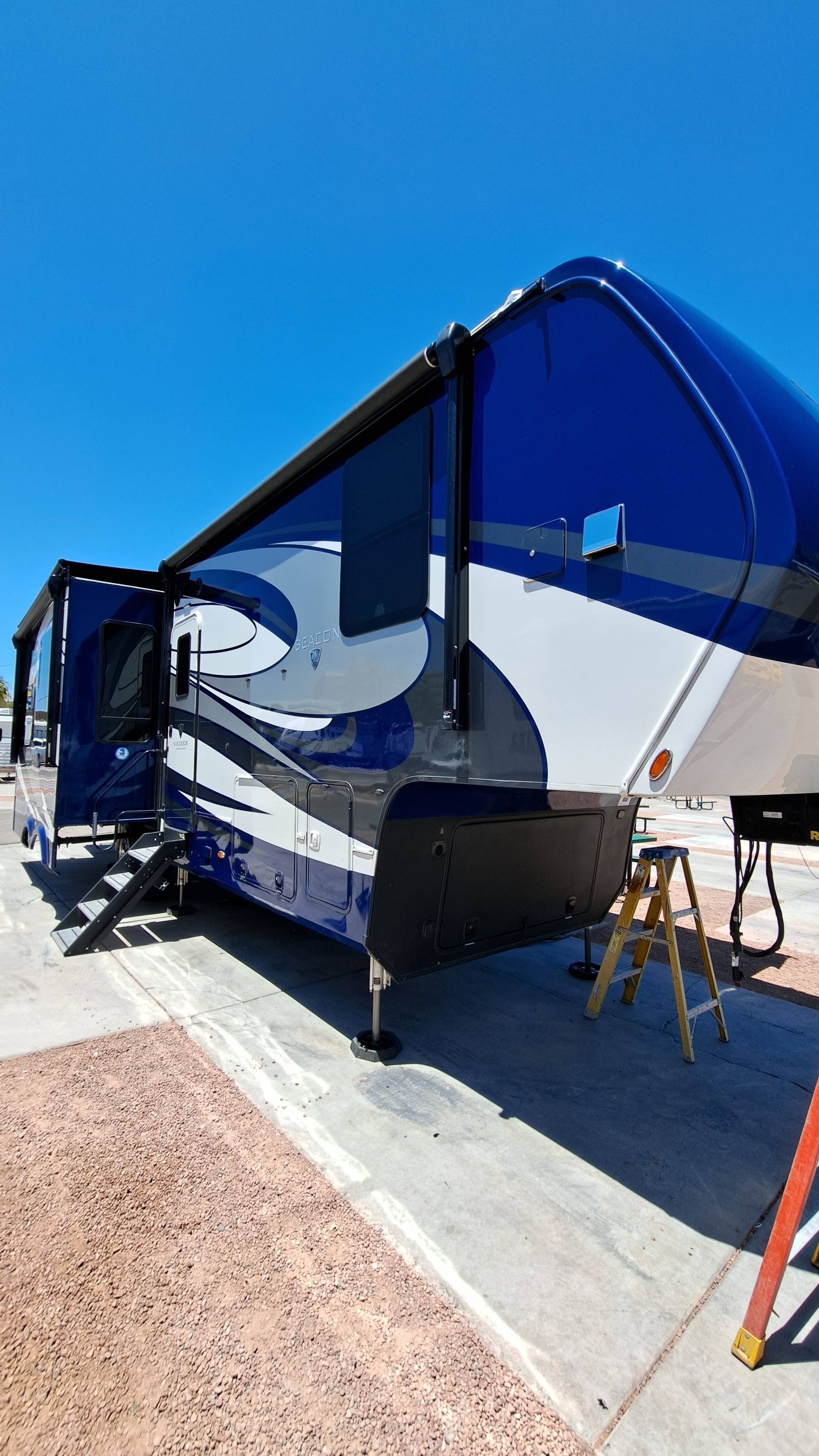 A blue and white rv is parked on the side of the road next to a ladder.