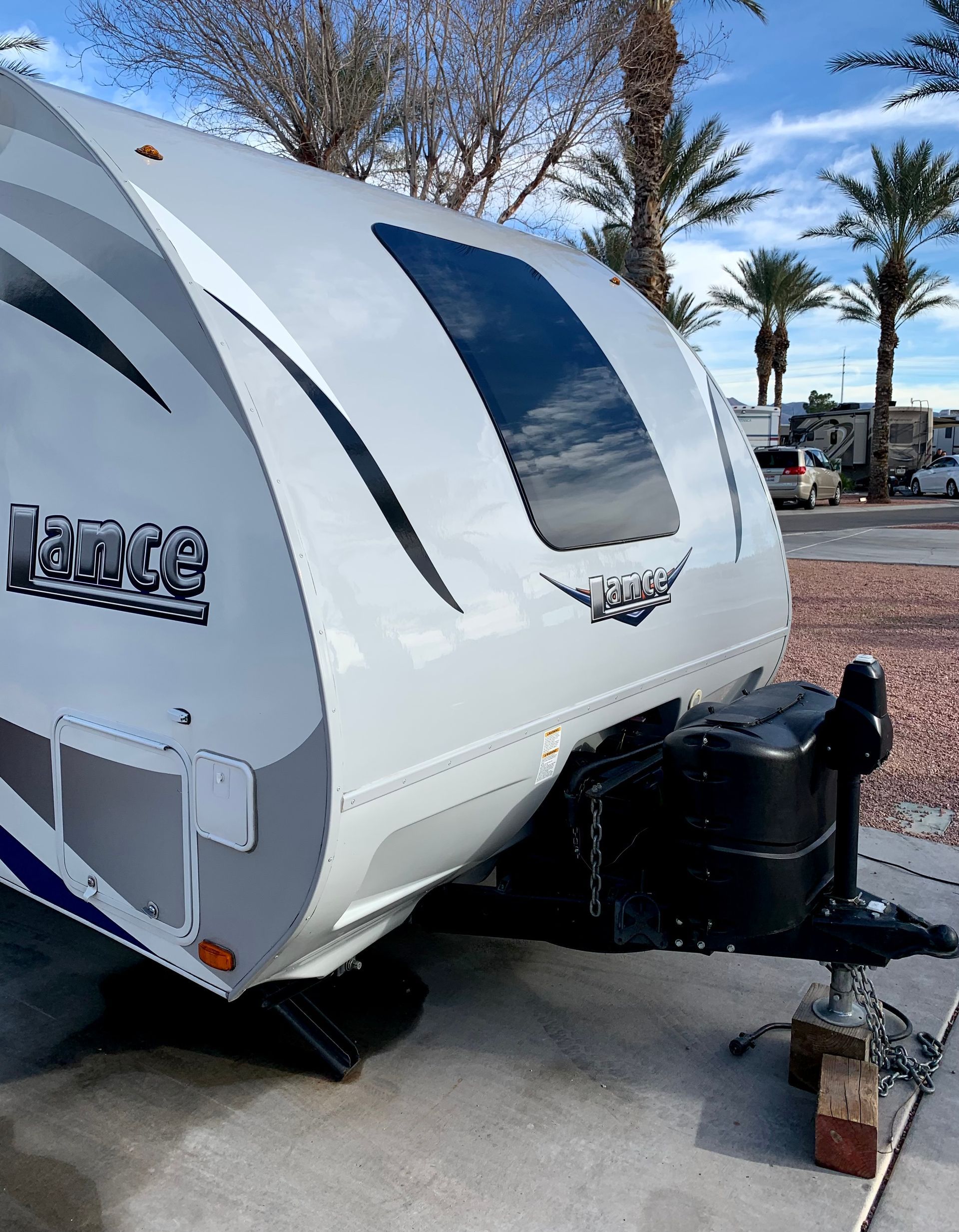 A white rv is parked in a parking lot with palm trees in the background.