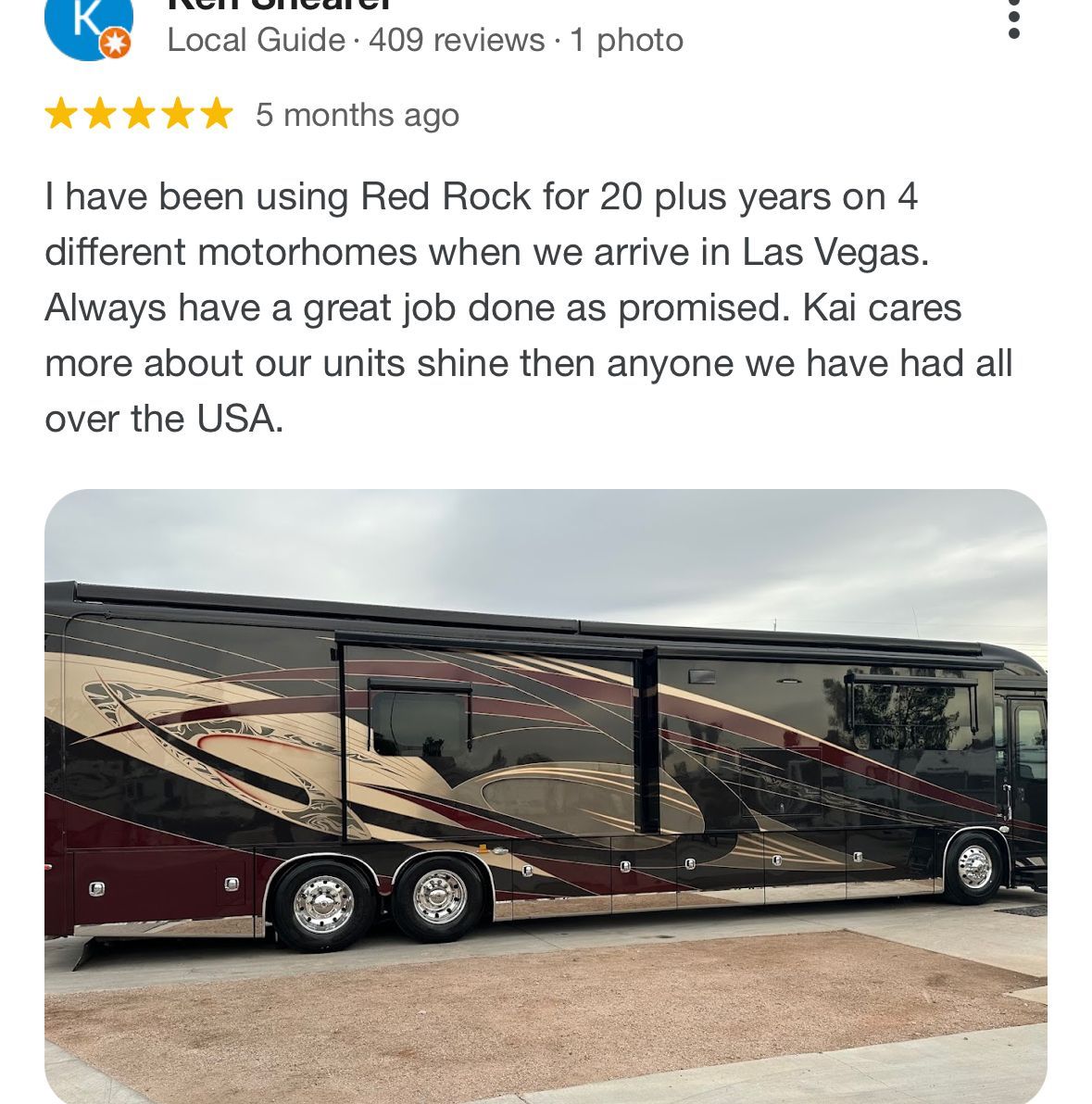 A red rock motorhome is parked on the side of the road.