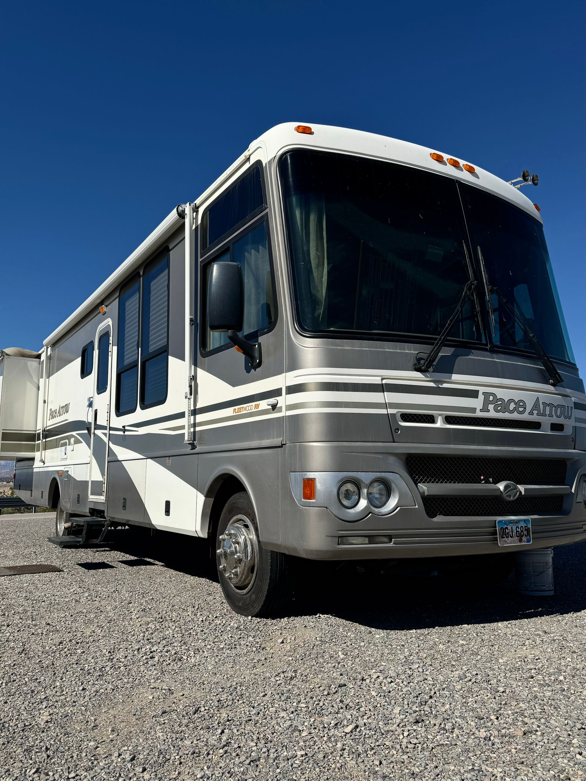 A silver and white rv is parked in a gravel lot.