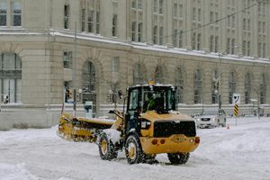 A yellow snow plow is driving down a snow covered street.