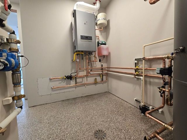 A room with a lot of pipes and a boiler on the wall.