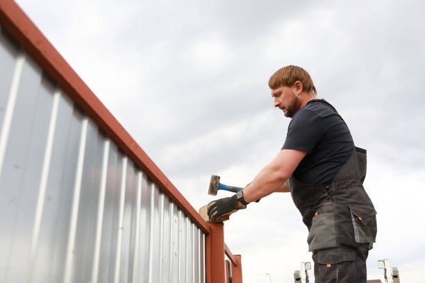 A residential fence contractor, wearing a dark uniform, is installing a fence near a house