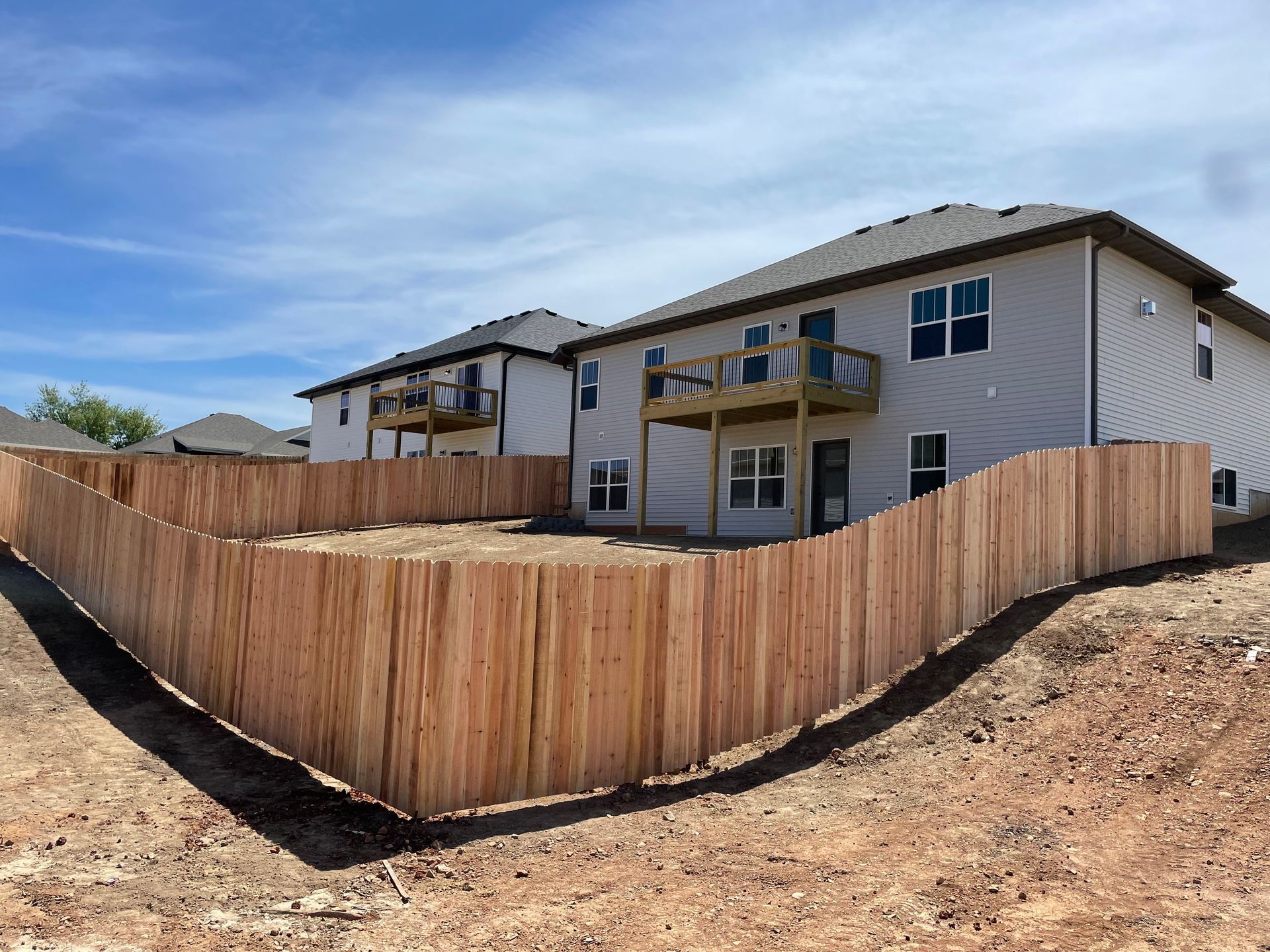 Black and white fence with vertical slats, set in front of a home with trees.