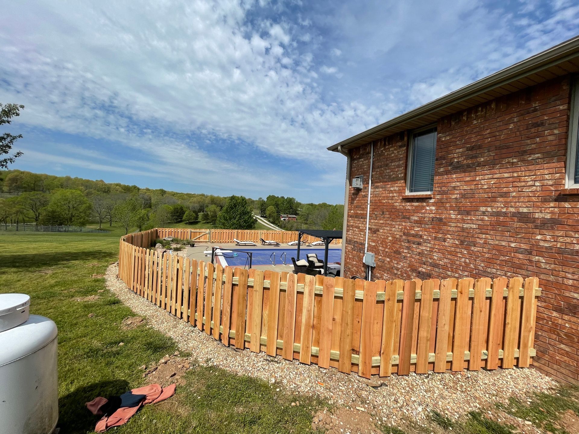Woman taking photo of gray house behind wooden fence.