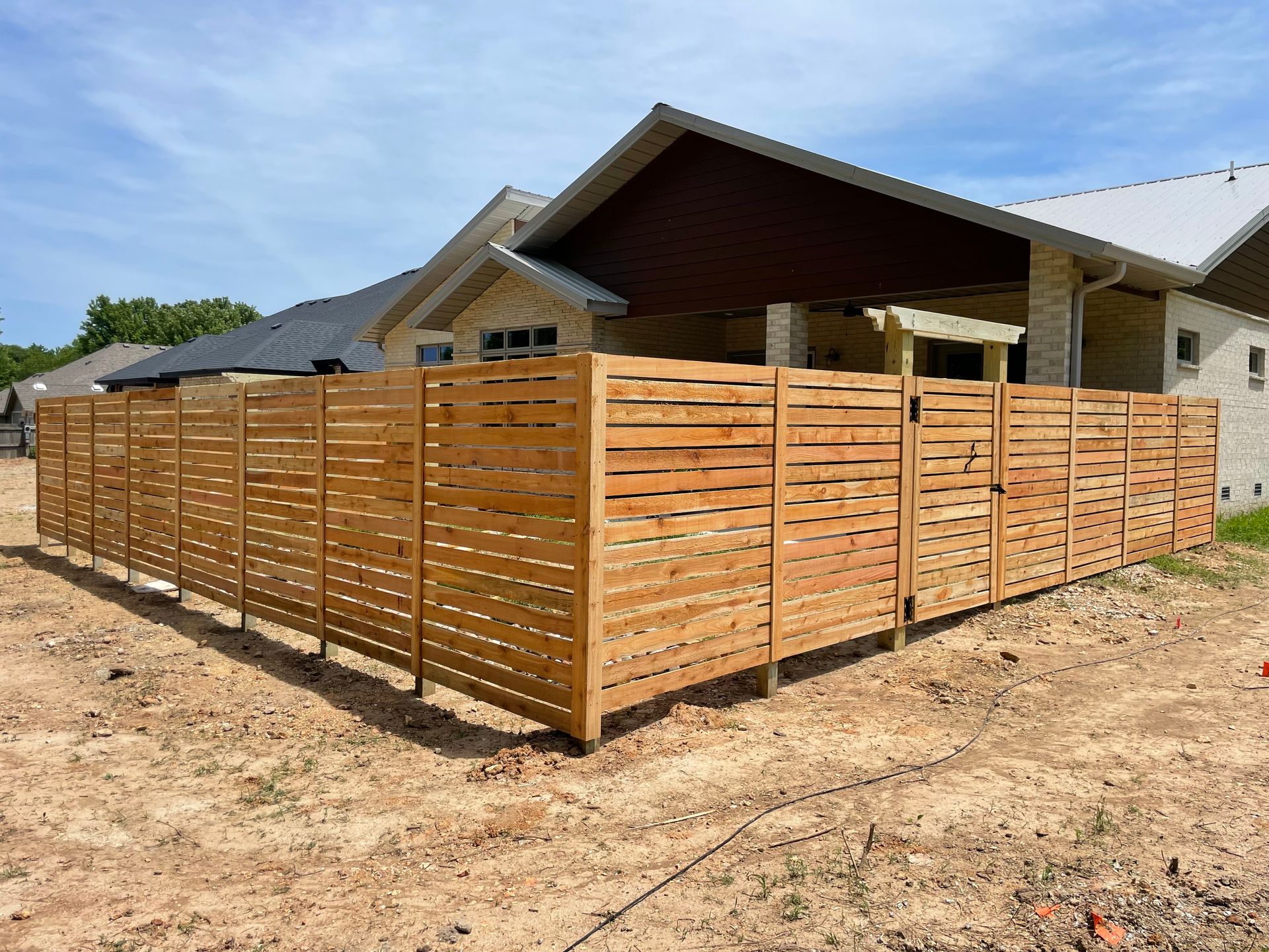 Black wrought iron gate in front of a lush green garden and modern buildings.