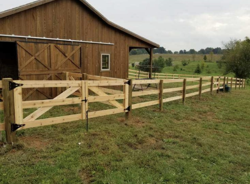 Farm with a white barn, silos, and a white fence on a green field under a blue sky with clouds.