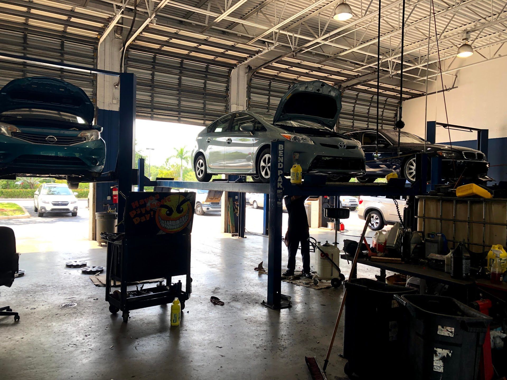 Cars on lifts in a mechanic's garage; a person is working on one. | Brake World