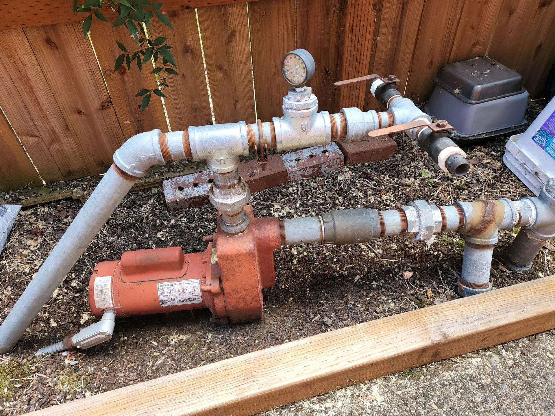 A bunch of pipes are sitting on the ground next to a wooden fence.
